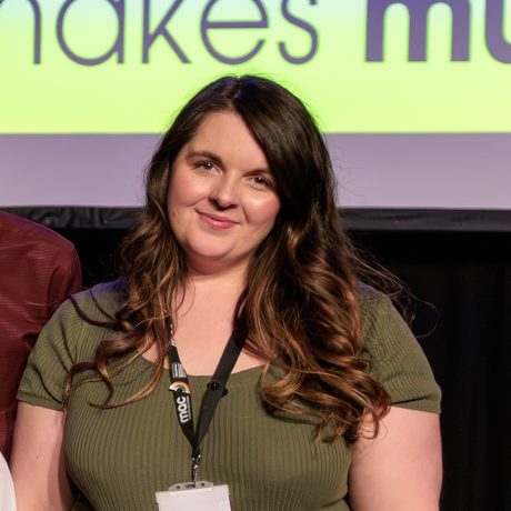 Julia Thomson-Smith smiling at the camera. She is wearing a green top and has long brown hair.