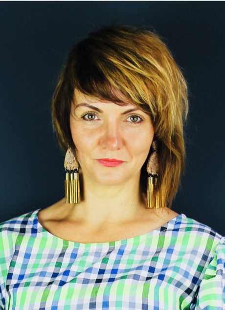 Michelle is facing the camera, wearing a green and blue plaid top and dangly earrings.