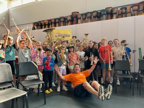 Helen Minshall sat on the floor waving her arms in the air, in front of a group of children all holding instruments in the air