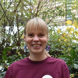 Laura Hailstone wearing a Music Mark t-shirt with a blonde fringe smiling at the camera, with foliage in the background.