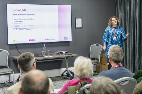 Liz Stafford stood in front of a presentation screen speaking, wearing a blue patterened dress