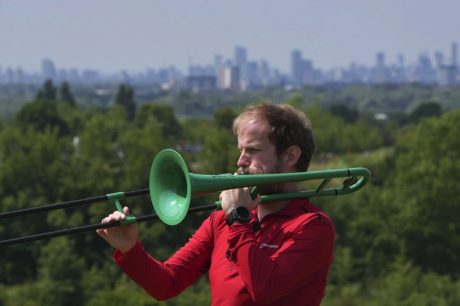 Nathaniel Dye playing a green plastic trombone outside