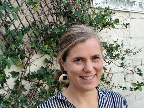 Anna Bull smiling, with a leafy trellis in the background