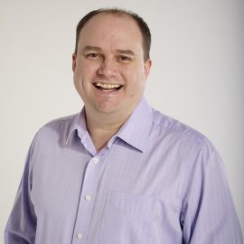 Steven Greenall smiling at the camera wearing a blue shirt