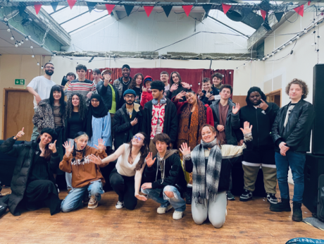 A group of young people stood indoors smiling and waving at the camera