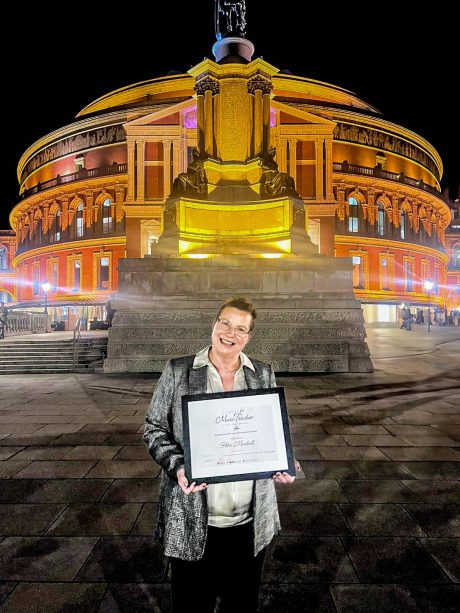 Helen Minshall holding a certificate stood in front of the Royal Albert Hall at night