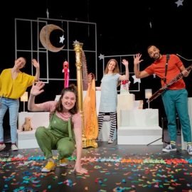 Four people smiling and waving surrounded by a variety of instruments and nighttime images.